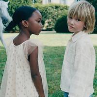 Image 3: Two children in a garden, one in a light dress with tulle and the other in a white shirt. A white horse can be seen in the background.