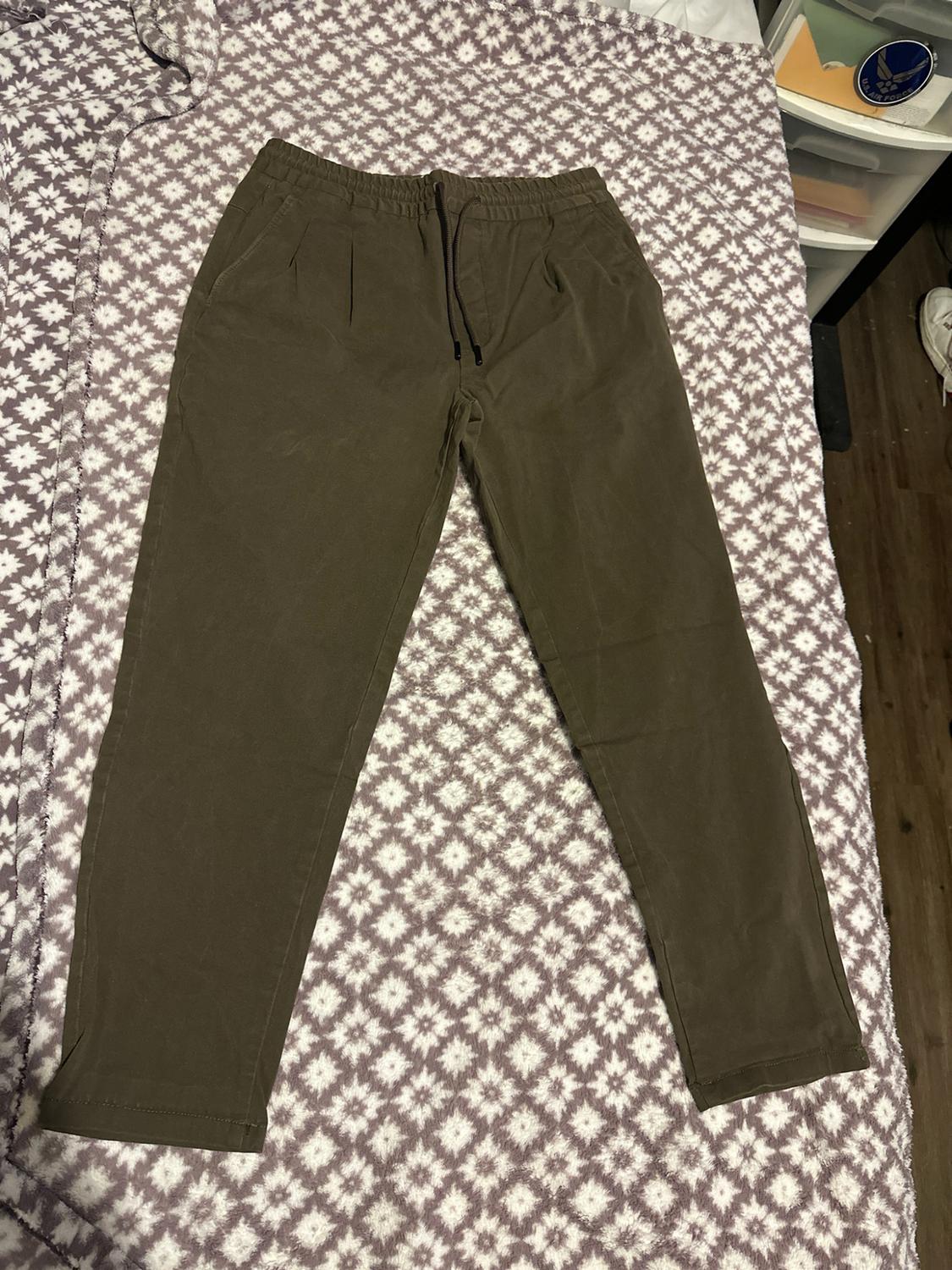 Olive green pants with an elastic waistband and drawstring, laid out on a white blanket with a pattern of purple stars.