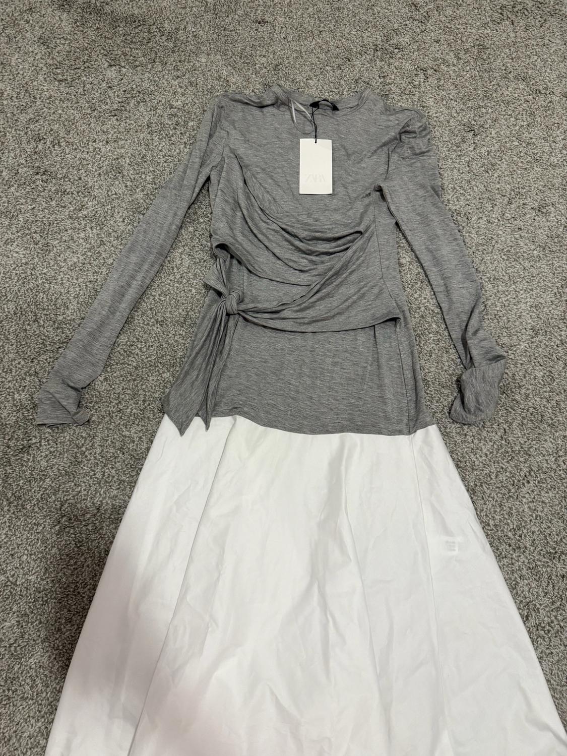 Dress with a gray long-sleeve top with a tied detail at the waist and a white skirt, with a Zara label, on a gray rug.