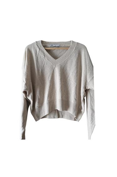 Loose-fitting beige knitted jumper with a V-neck, hanging on a wooden hanger against a white background. ZARA label visible.