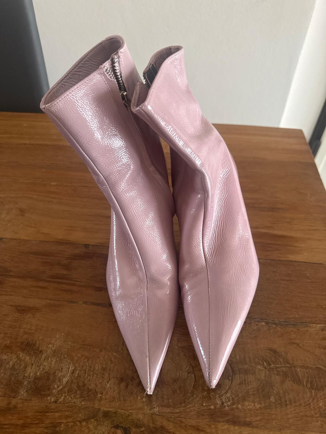 Pink patent leather ankle boots with pointed toes and a side zip, placed on a wooden table.