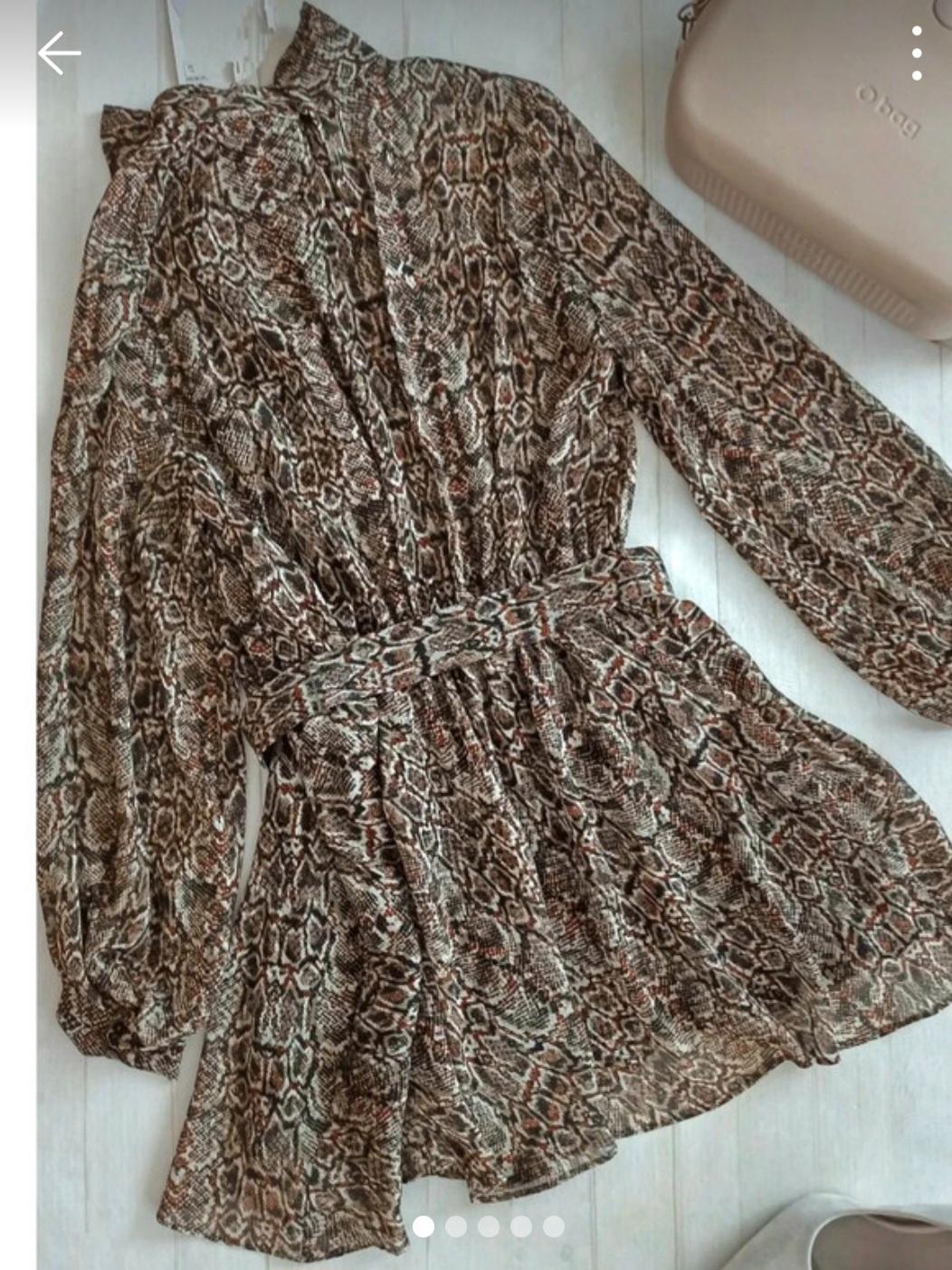 Dress with a snake print in brown and beige tones, with long sleeves and a matching belt, against a white background. Beige handbag next to it.