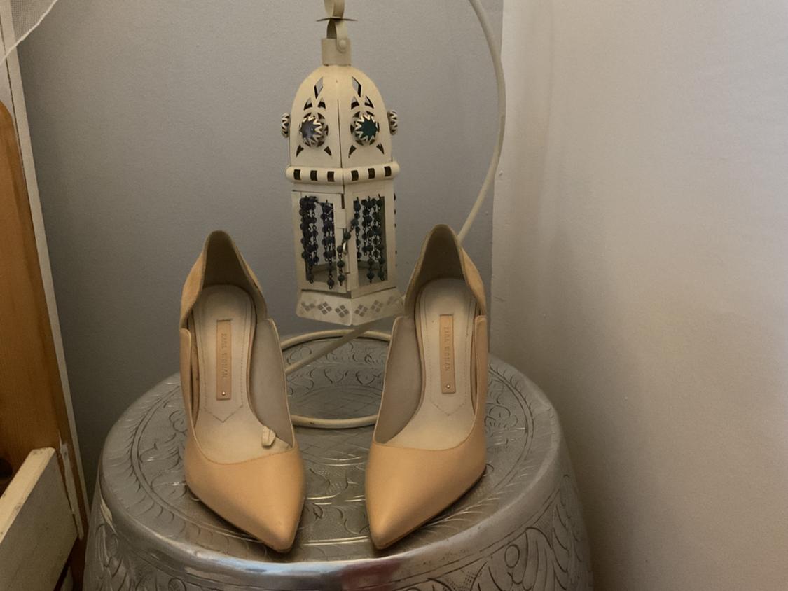 Front view of beige closed-toe high-heeled shoes on a decorative table.