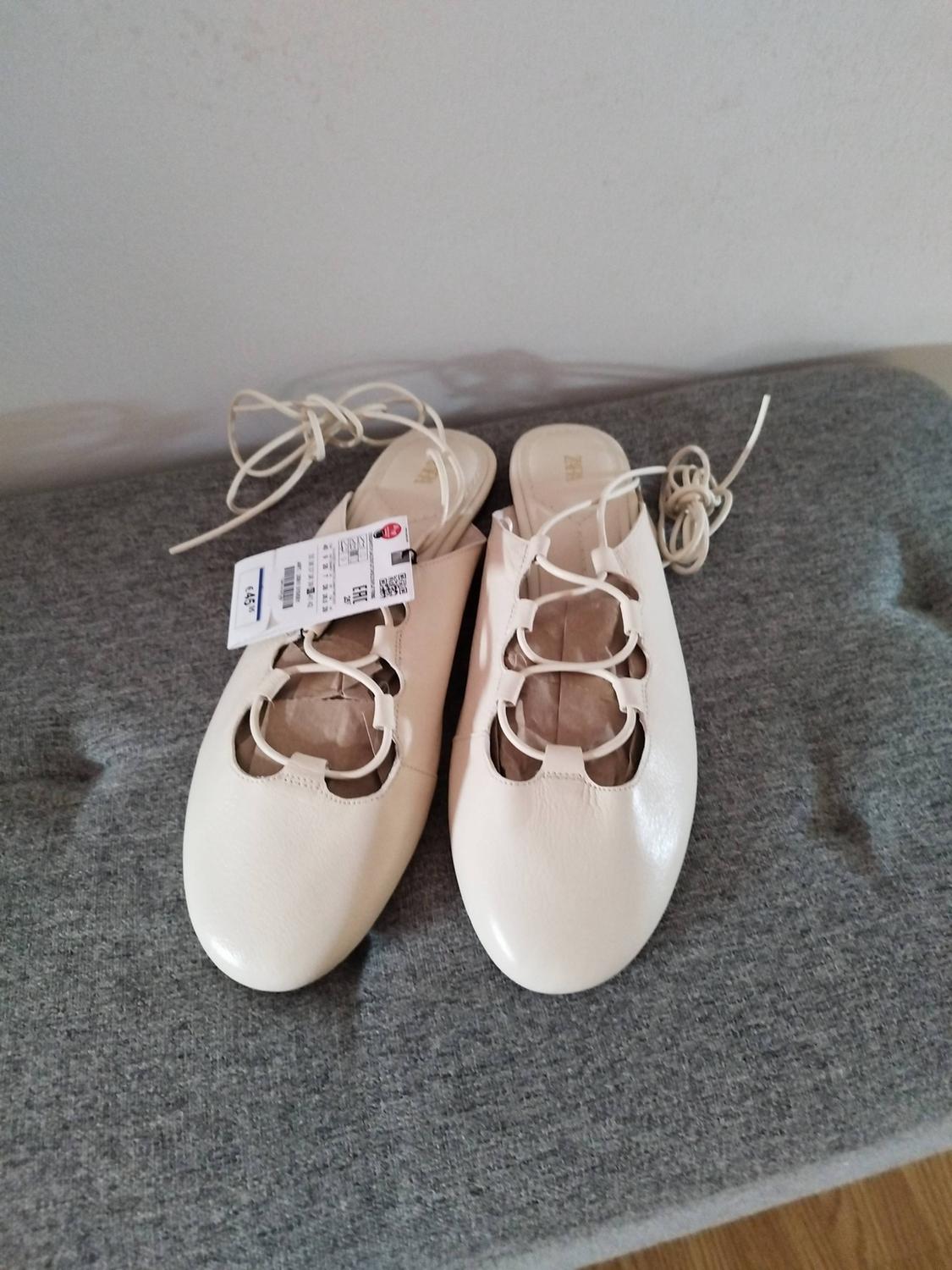 Cream-coloured lace-up flats on a grey cushion. Relaxed atmosphere. Label with ZARA text and € 45.95.