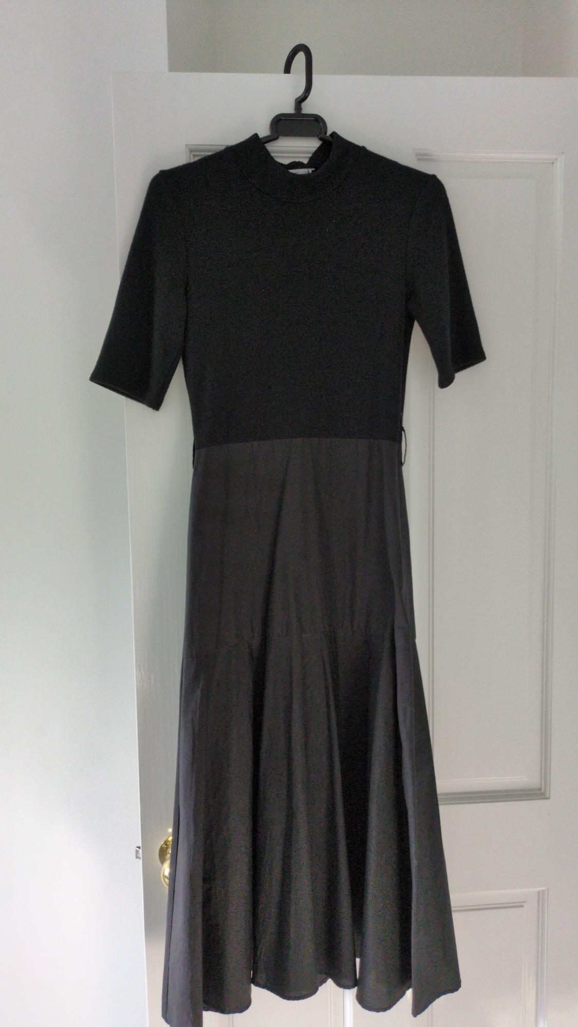 Short-sleeved black dress with a high neck and flared skirt, hanging on a coat hanger over a white door.