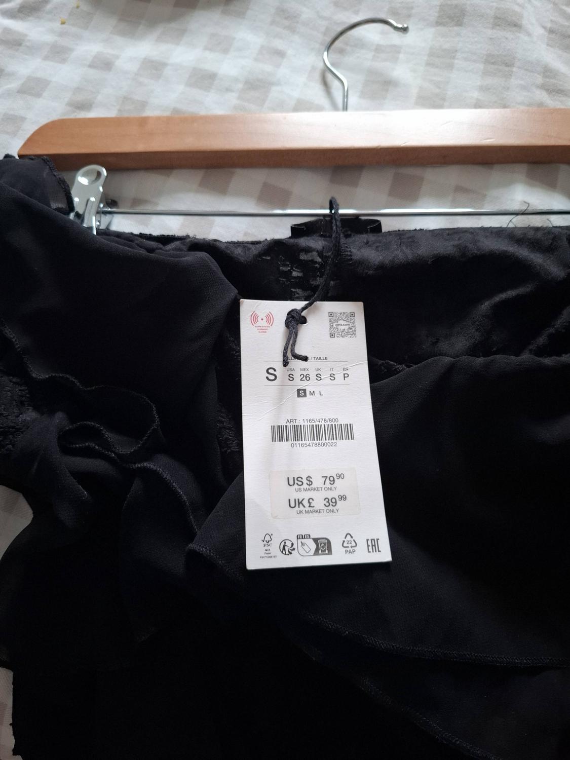 Black garment with frills on a hanger. Label: ART.: 1165/478/800 01165478800022 US $79.90 US MARKET ONLY UK £39.99 UK MARKET ONLY