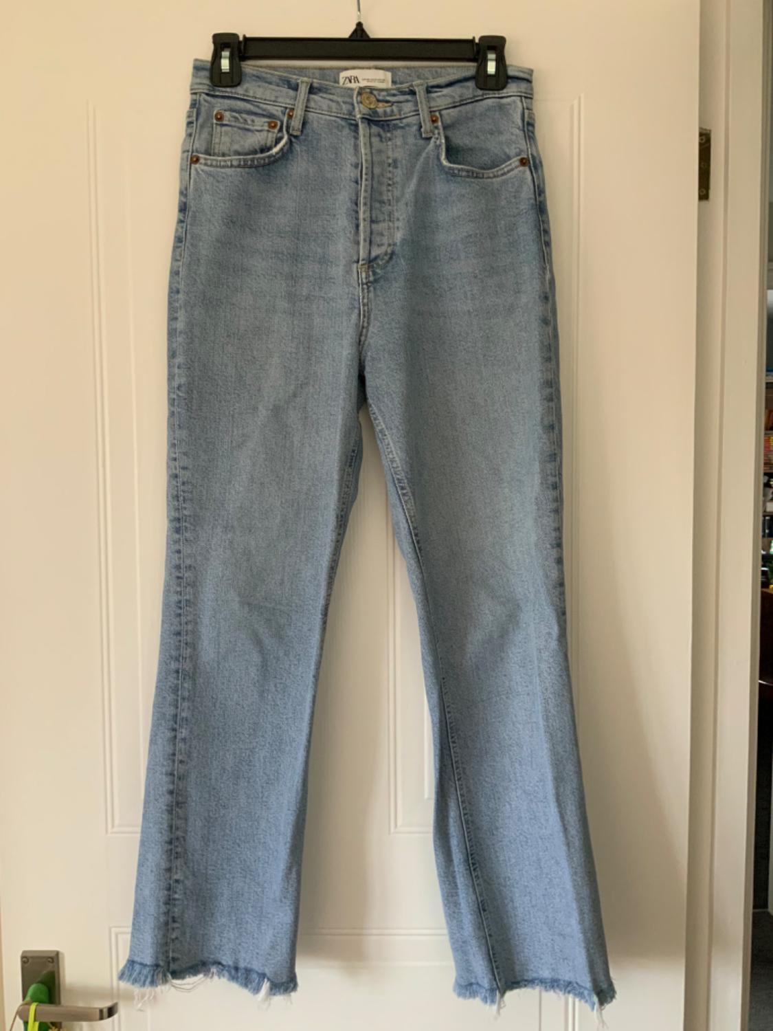 Front view of light blue jeans with front pockets and frayed hems.
