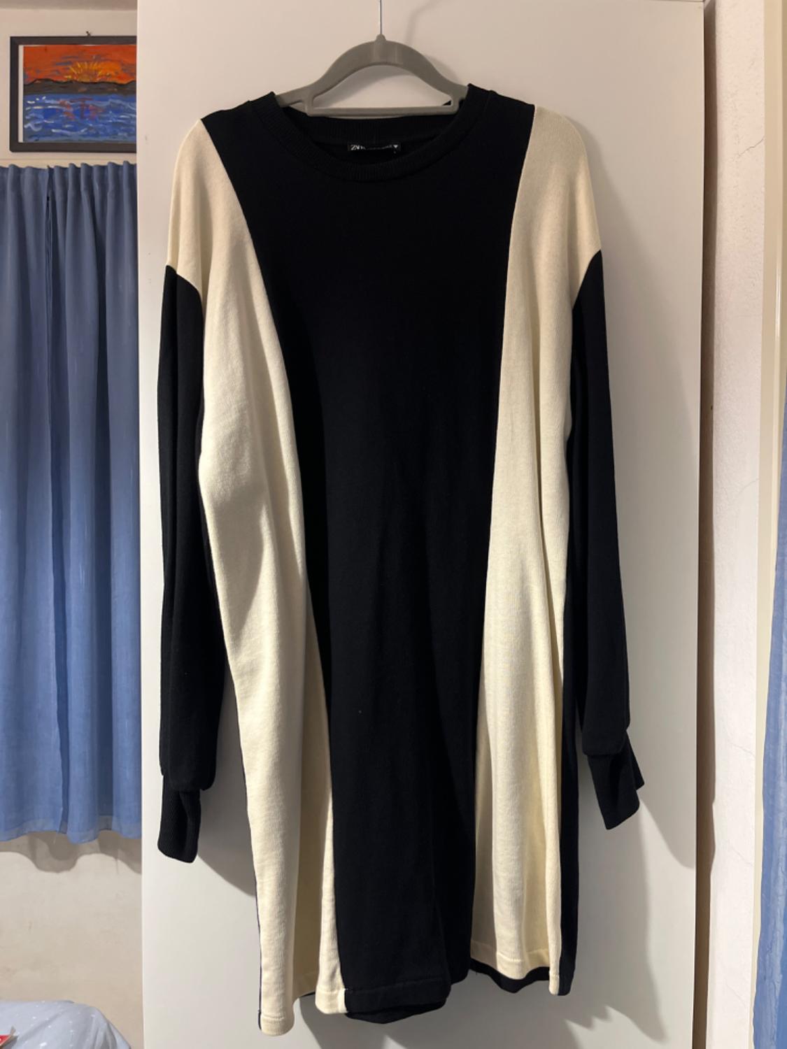 Black and white colourblock knitted dress, hanging on a hanger over a white door. Against a blue curtain in the background.