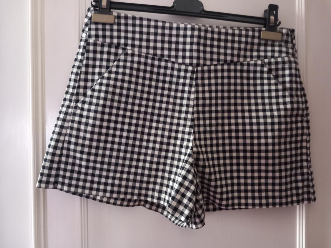 Black and white gingham shorts with side pockets, hanging on a black hanger in front of a white door.