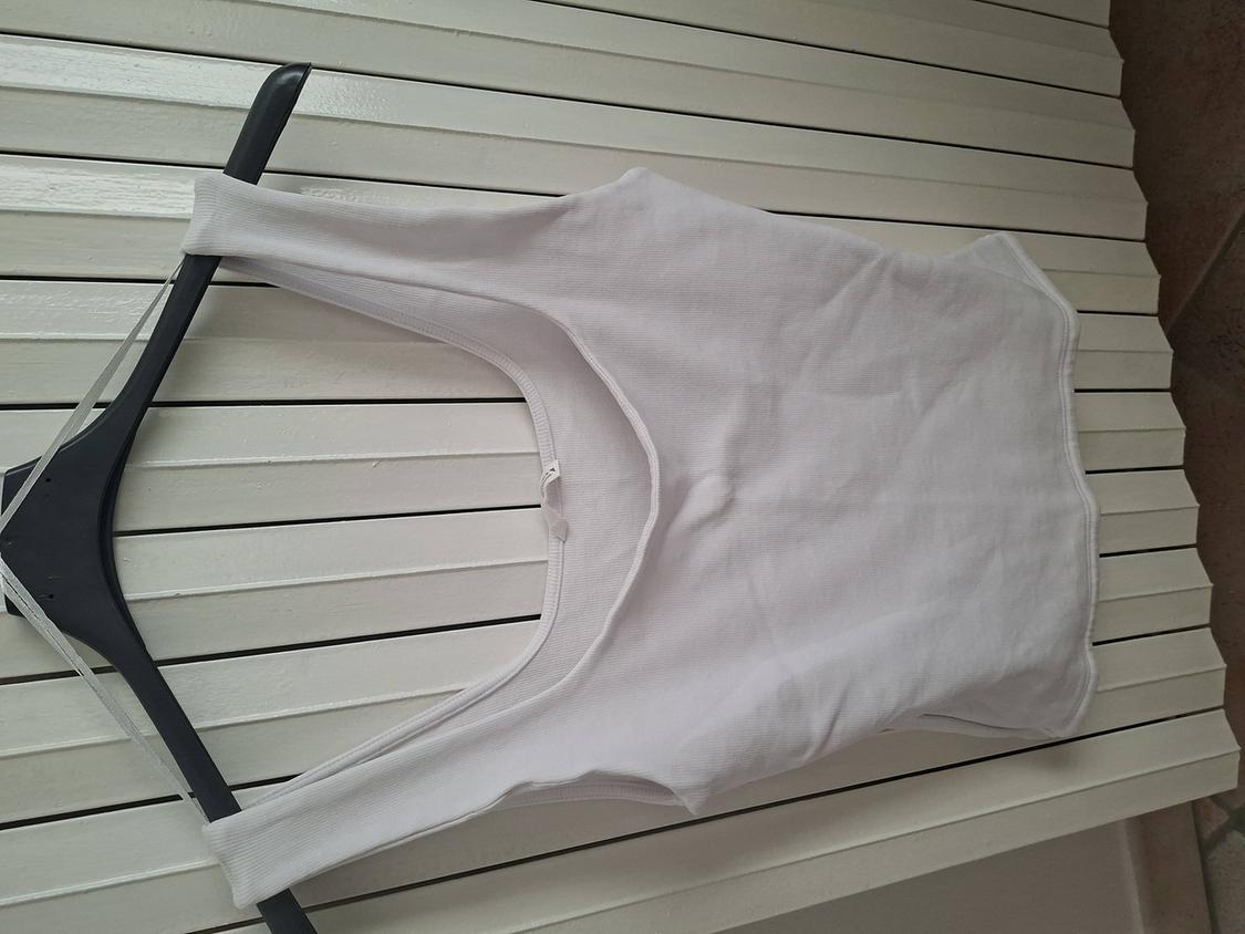 White sleeveless top hanging on a black hanger against a white slatted background.