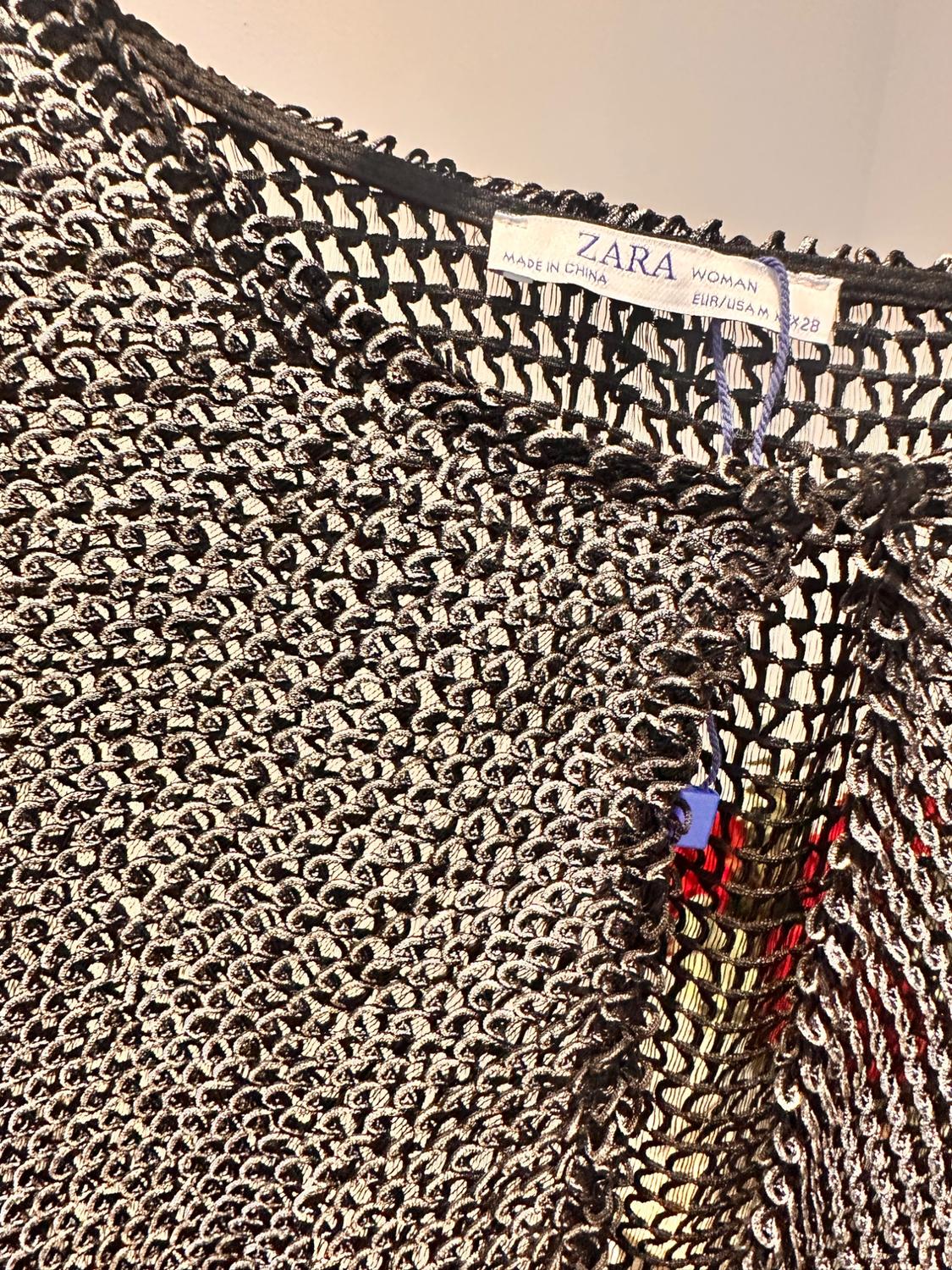 Close-up of a chunky knit fabric in dark tones with a visible label that reads "ZARA WOMAN, MADE IN CHINA, EUR/USA M".