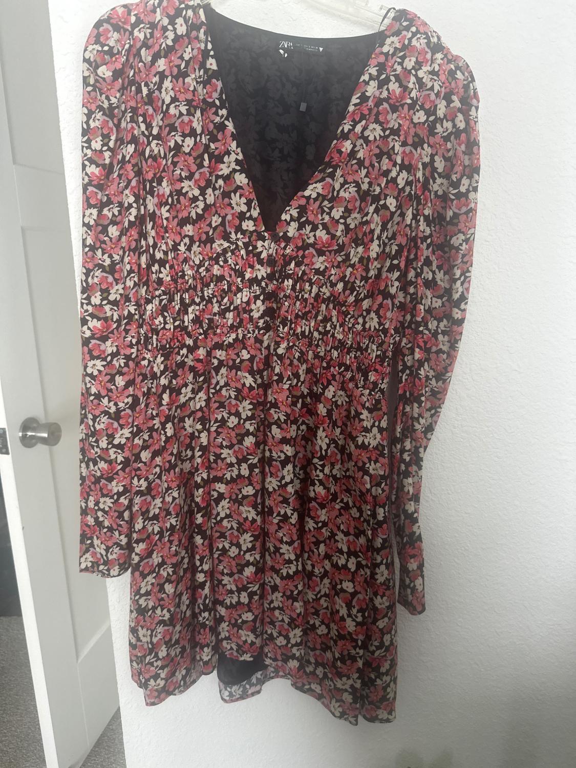 Long-sleeved floral dress with a black background and red and white flower print, hanging on a hanger over a white door.