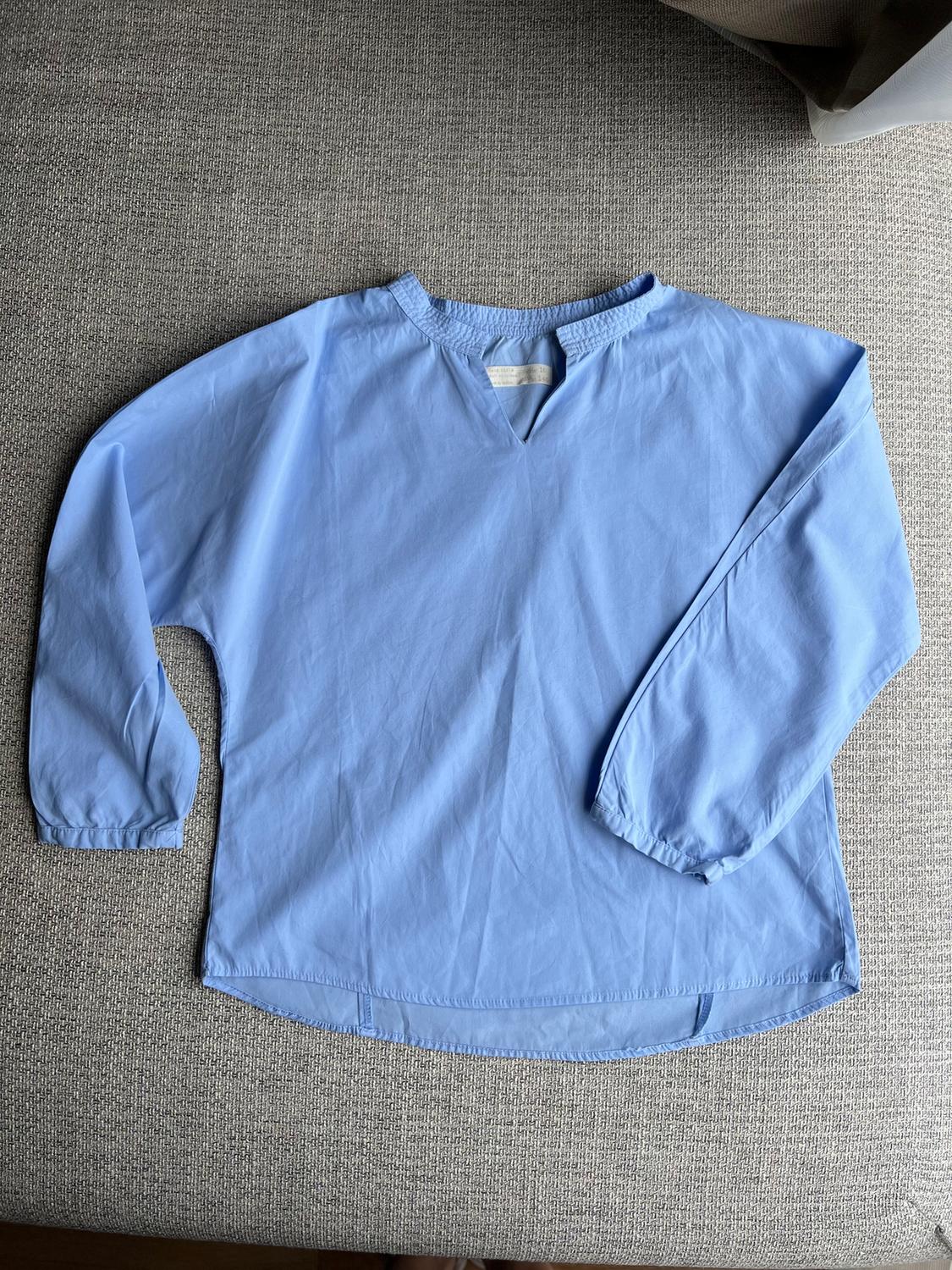 Light blue, long-sleeved V-neck shirt, laid on a grey fabric background.