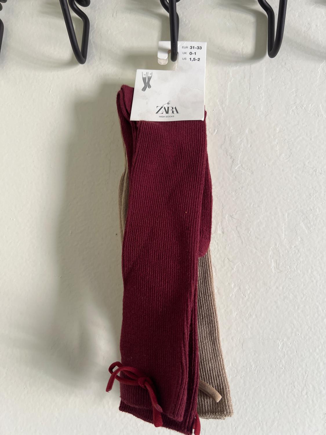 Burgundy and beige knee-high socks hanging on a hook. Visible label with sizes EUR 31-33, UK 0-1, US 1.5-2. ZARA brand.