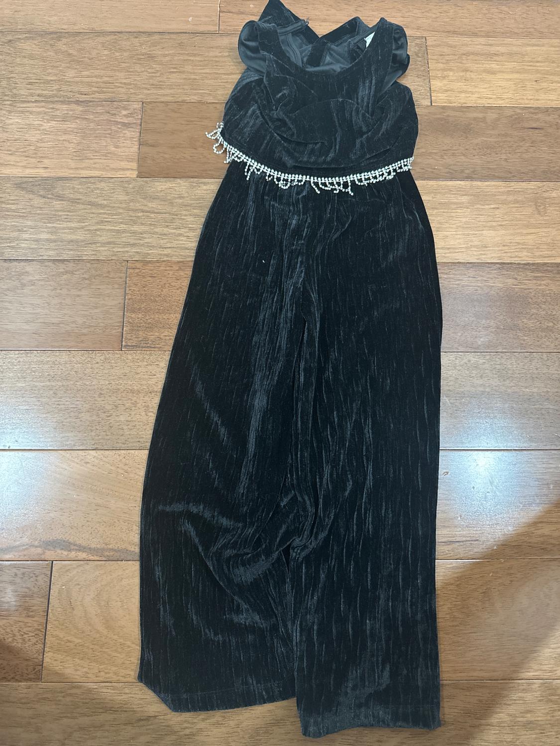 Black velvet dress with a gathered neckline and pearl detail at the waist, on a wooden floor.