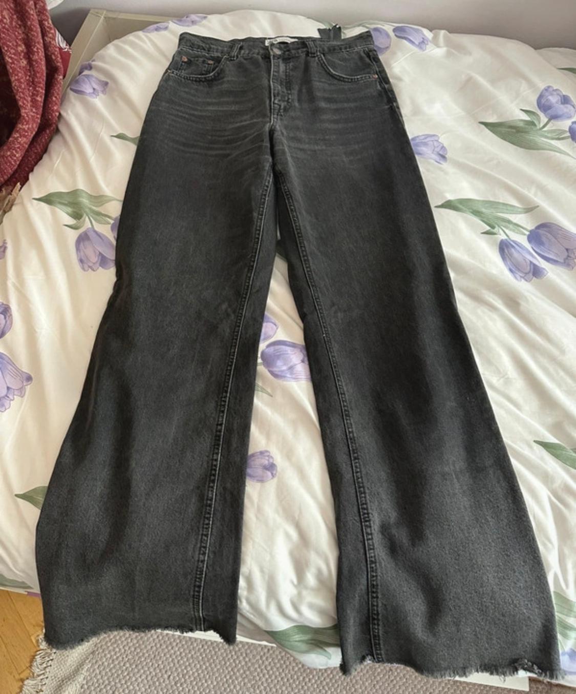 Black, wide-leg jeans with a frayed hem, placed on a bed with purple floral sheets.