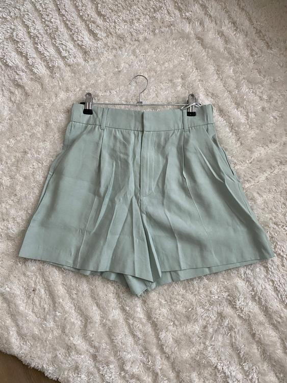 Light green shorts hanging on a hanger over a white furry textured rug.
