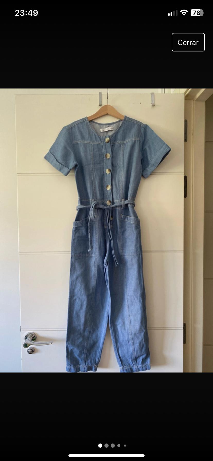 Front view of a blue jumpsuit with large buttons and a belt, visible side pockets.
