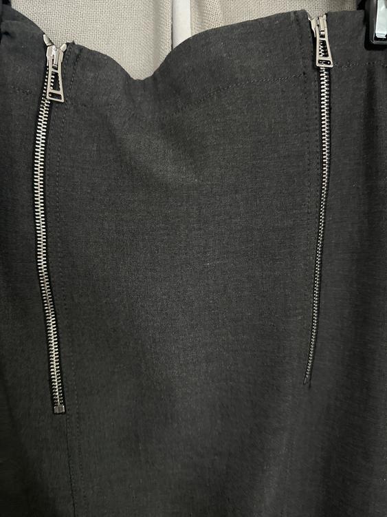 Gray skirt with two vertical metallic zippers on the front, hanging over a light background.