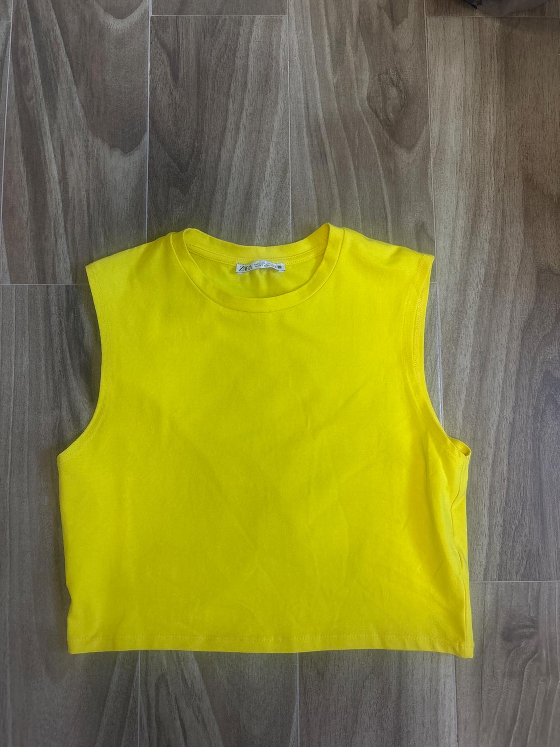 Yellow tank top on a wooden floor. The visible tag says "Zara."