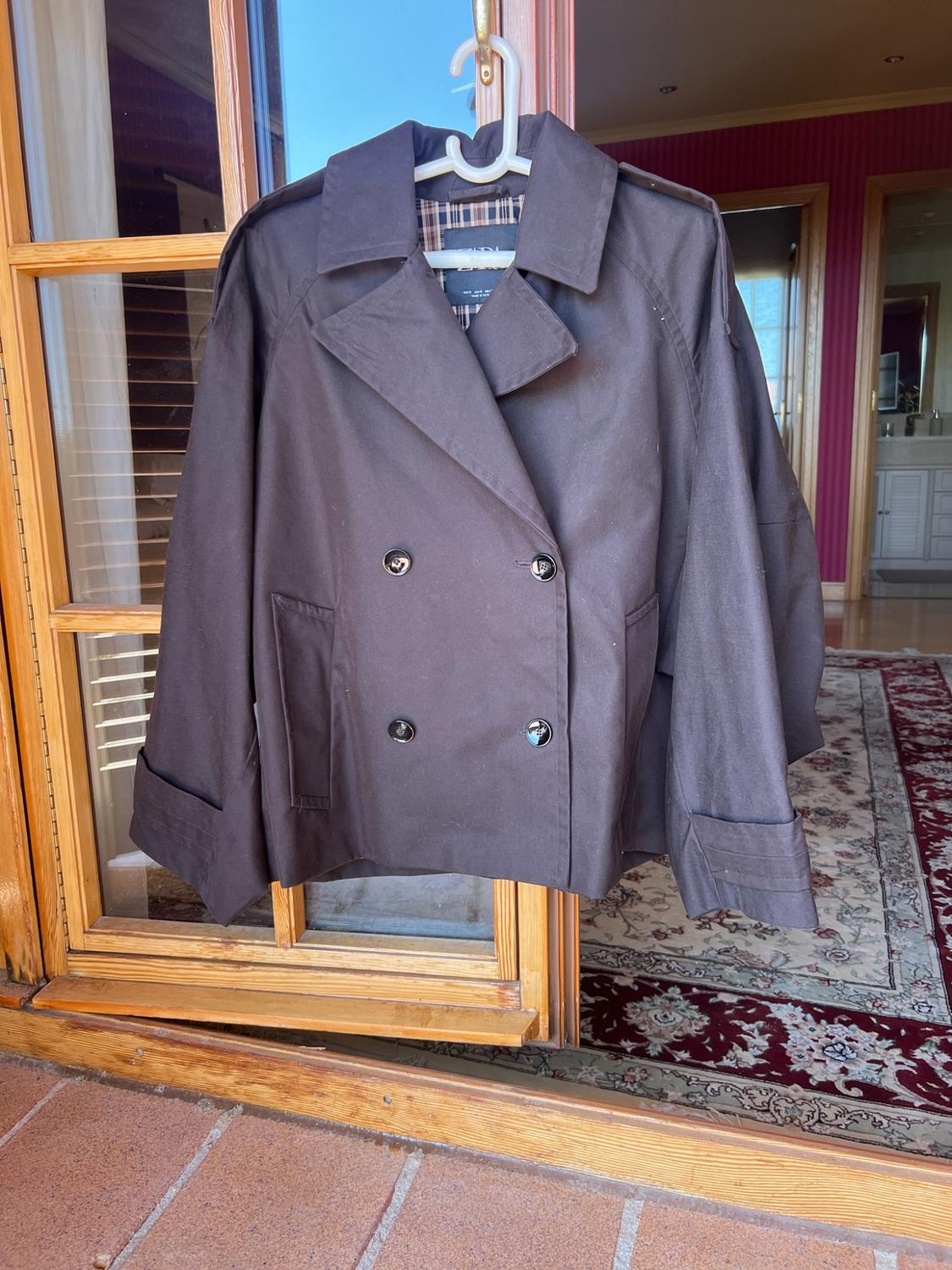 Dark double-breasted jacket with buttons hanging on an open wooden door. In the background, the interior of a house with a rug.