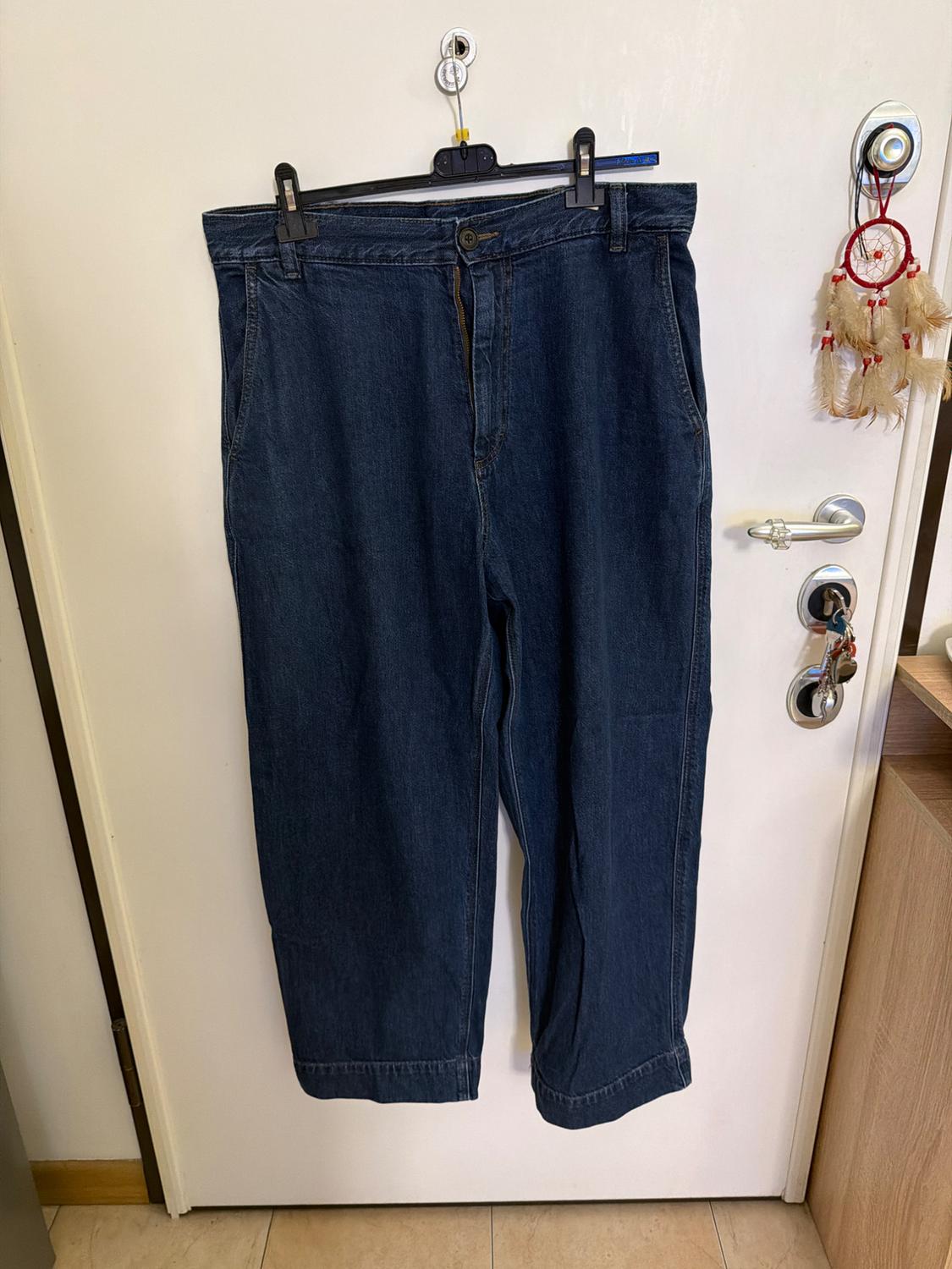 Dark blue denim trousers hanging on a black hanger over a white door, with a dreamcatcher next to it.