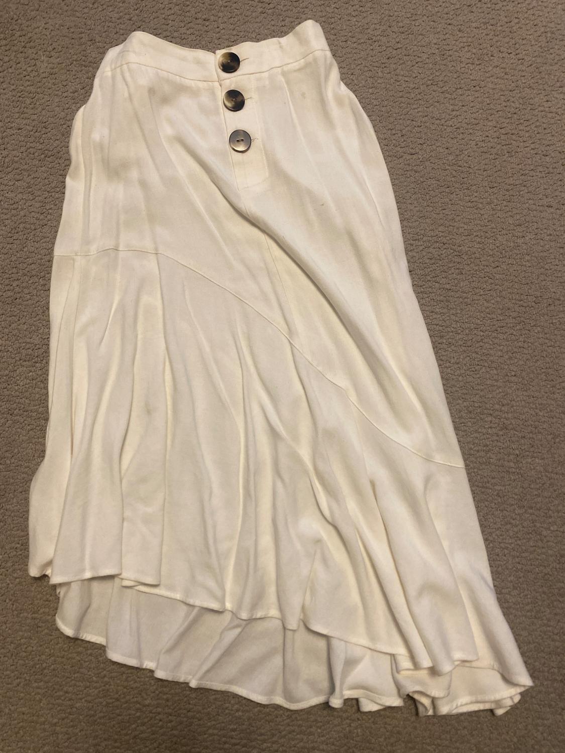 Front view of a white skirt with large buttons and pleats, asymmetrical at the bottom.