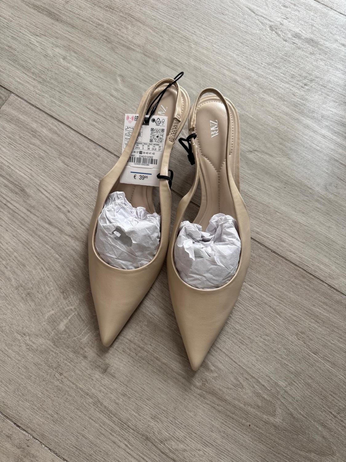 Beige pointed shoes with a price tag of €39.95 and tissue paper, on a light wooden floor. Visible brand: ZARA.