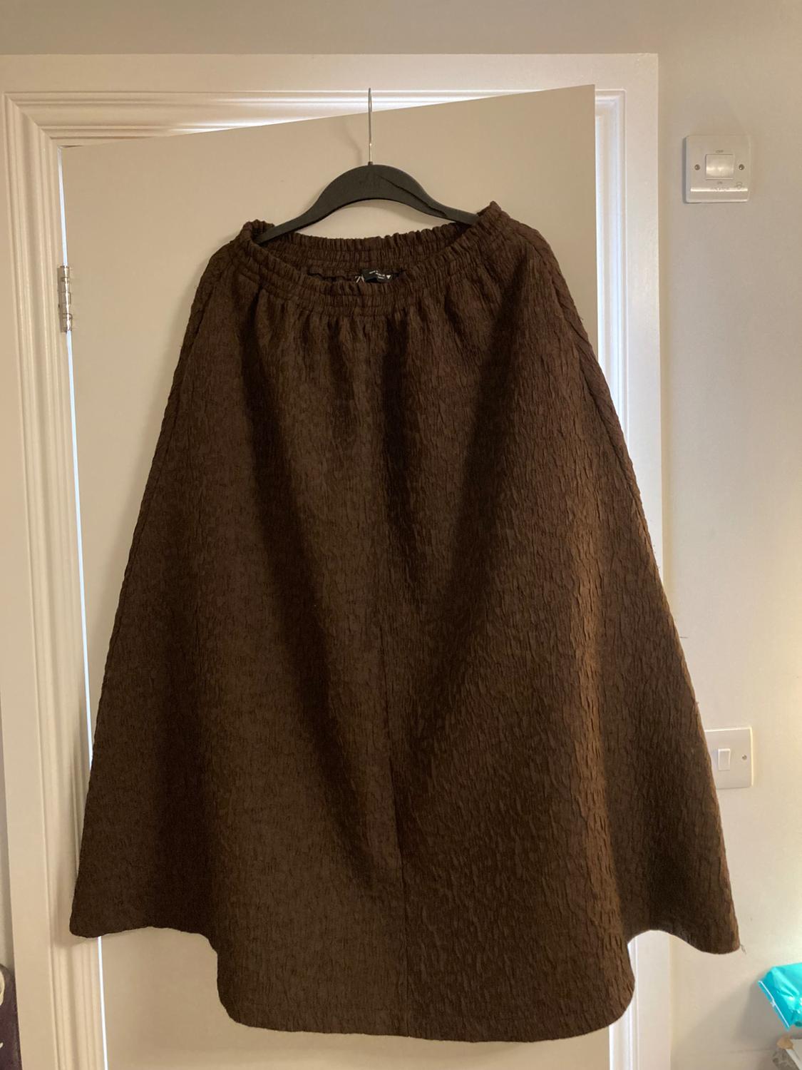 Textured brown skirt hanging on a black hanger over a white door. Indoor setting with soft light.