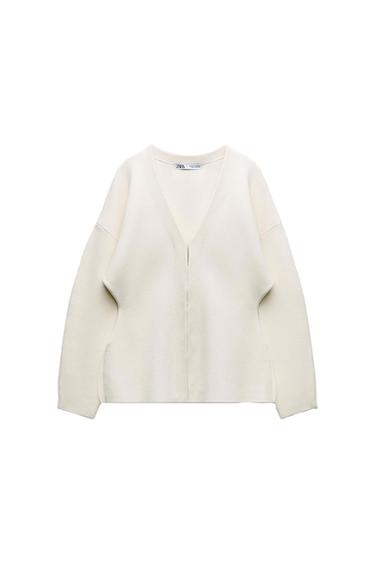 White long-sleeved cardigan with V-neck and loose fit. Visible label on the collar with text "ZARA". White background.