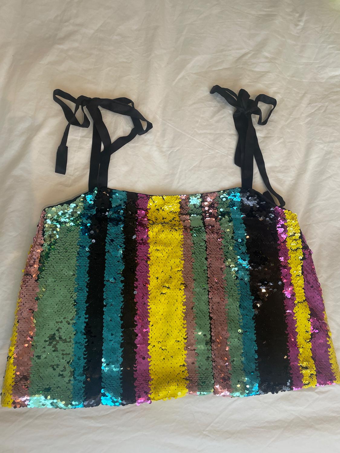 Multicoloured vertical striped sequin top with black straps on a crinkled white background.