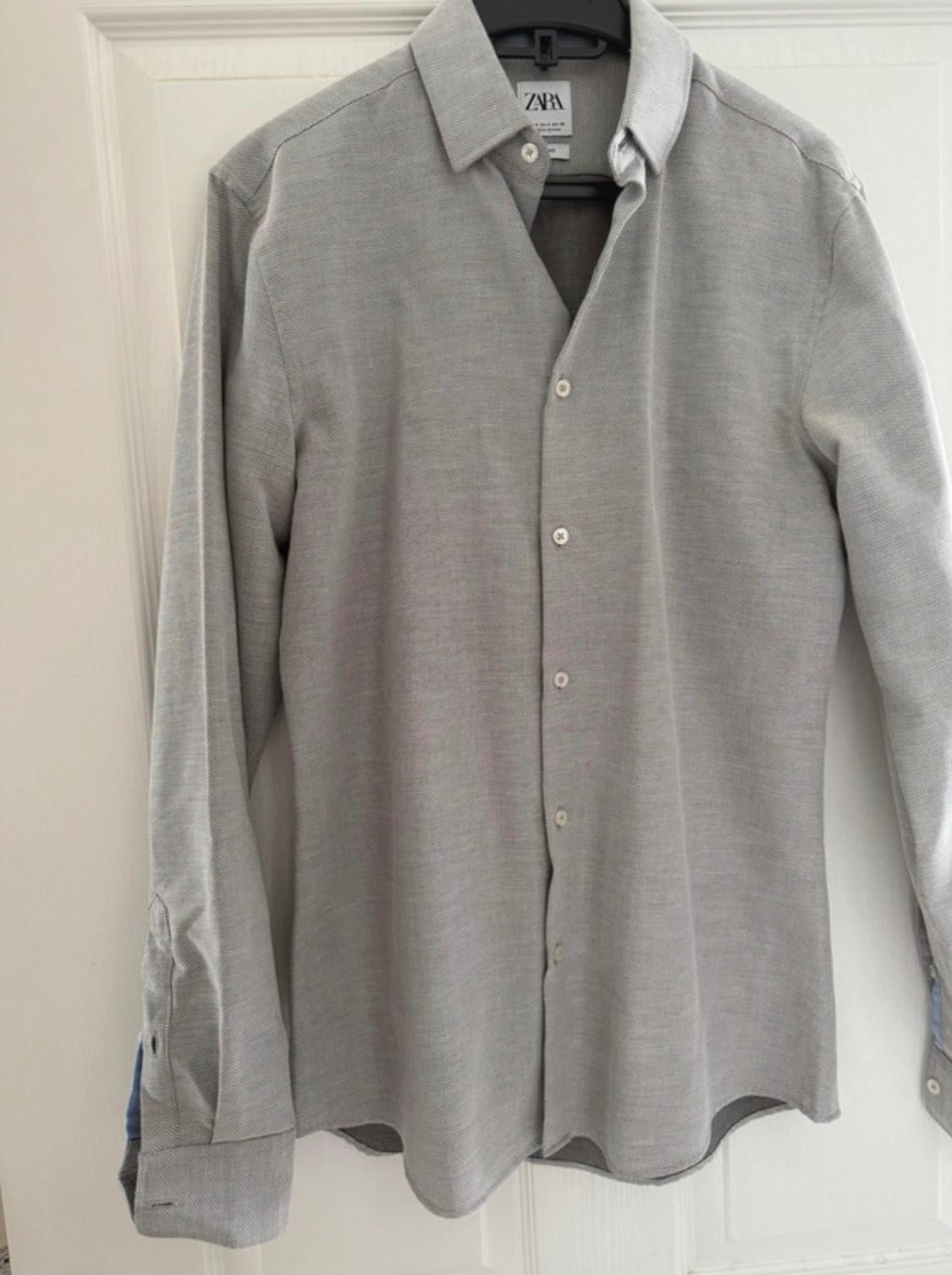 Grey long-sleeved shirt hanging on a black hanger. Visible 'ZARA' label on the collar.