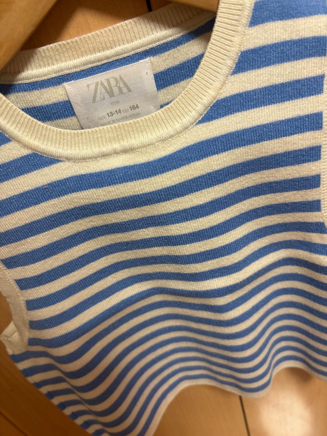 Blue and white striped sleeveless knitted top on a hanger. Text: ZARA KIDS SIZE 13-14 CM 164 MADE IN BANGLADESH.