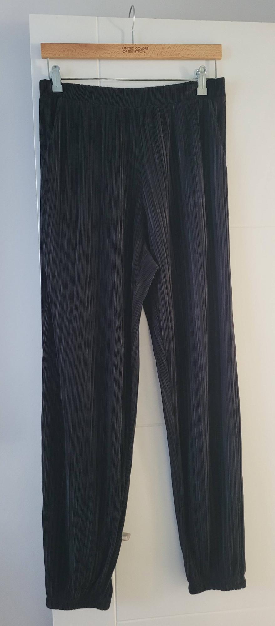 Black pleated trousers hanging on a wooden hanger with the "United Colors of Benetton" brand visible at the top.