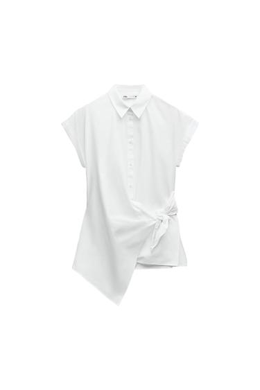 White shirt with a collar, short sleeves, buttons, a side knot, and an asymmetrical hem on a white background. Text: ZARA.