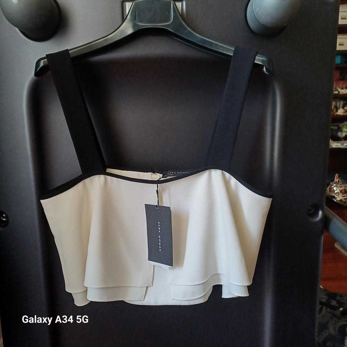 White top with black straps hanging on a black hanger. Visible label. Text on image: "Galaxy A34 5G".