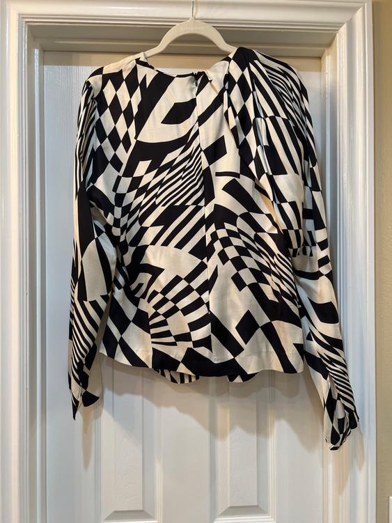 Blouse hanging on a door, with a black and white geometric print. Long sleeves and abstract design.