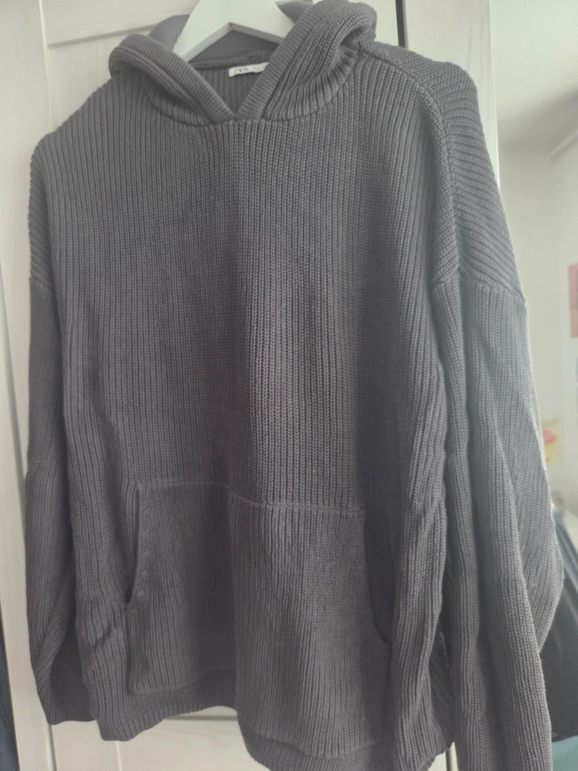 Dark grey ribbed-knit hoodie with a hood and kangaroo pocket, hanging on a white hanger against a light background.