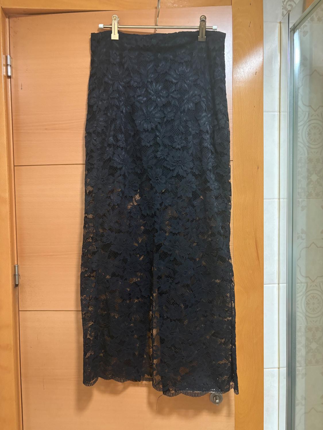 Long black lace skirt with sheer detailing, hanging on a hanger over a wooden door in an interior.