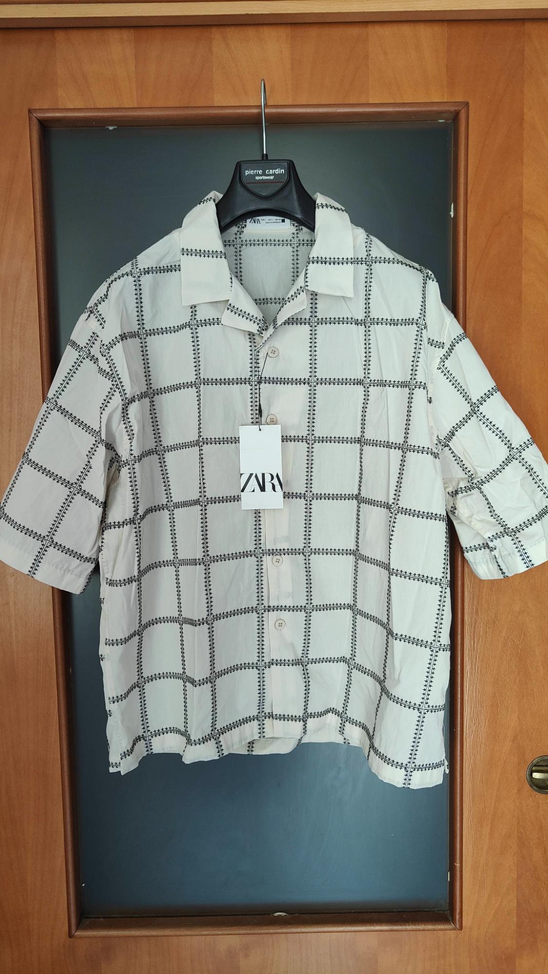 White short-sleeved shirt with a black check pattern hanging on a hanger. Visible text: ZARA and pierre cardin sportswear.