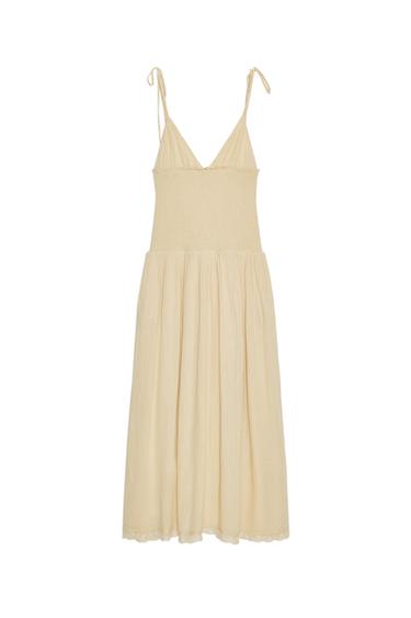 Front view of a beige midi dress with a V-neck, thin straps with tie fastening, and elasticated honeycomb-style fabric.