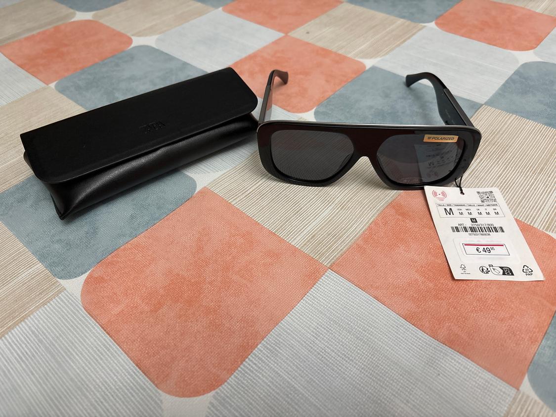 Black sunglasses with a €49.95 price tag, next to a black case on a colourful checked tablecloth.