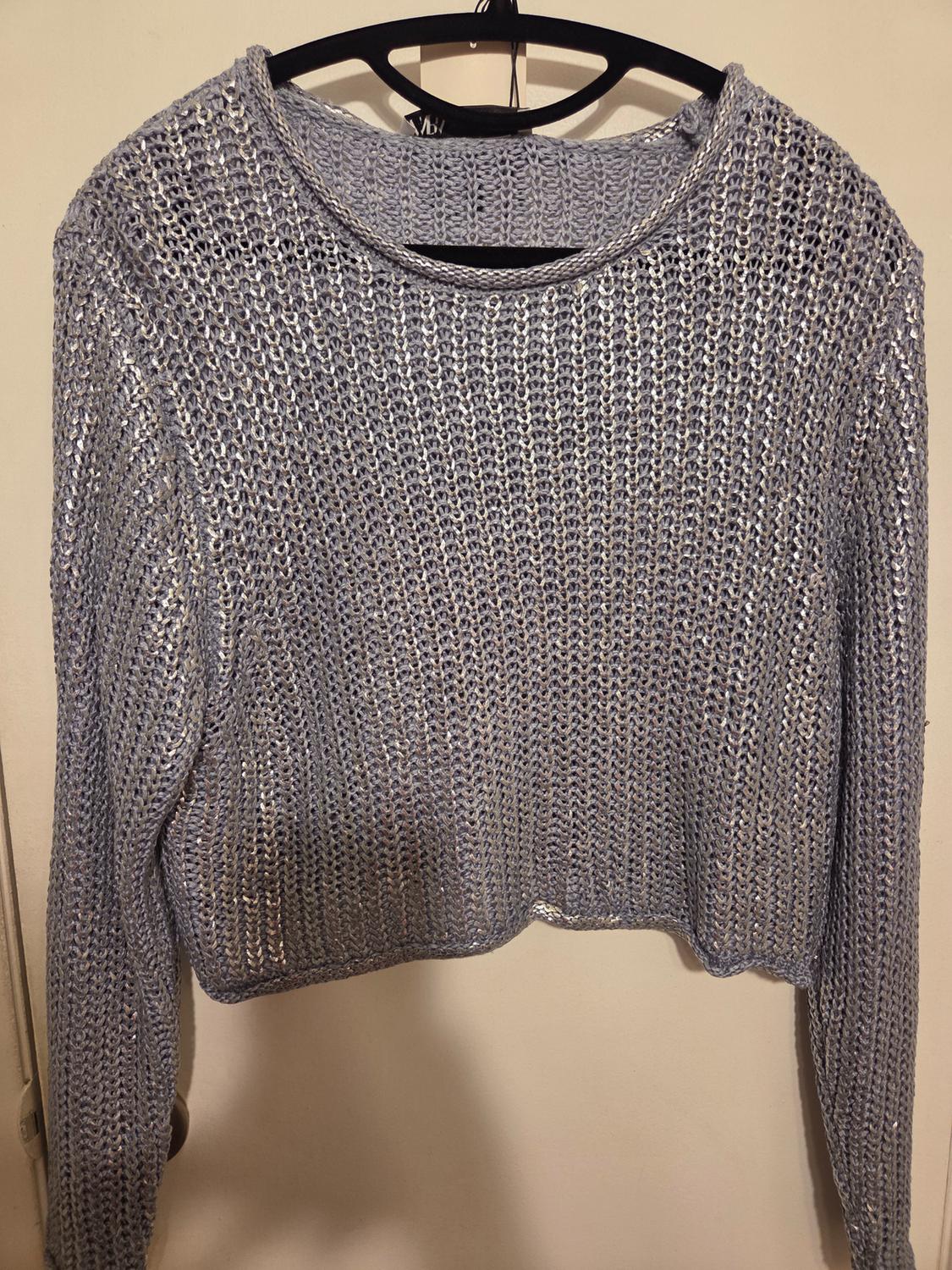 Metallic gray long-sleeved knitted sweater, hanging on a black hanger against a beige background.