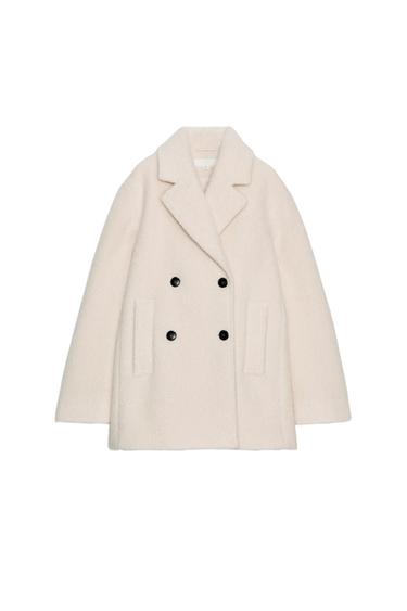 Front view of a beige double-breasted mid-length coat with a lapel collar, long sleeves, jetted front pockets, and black buttons.