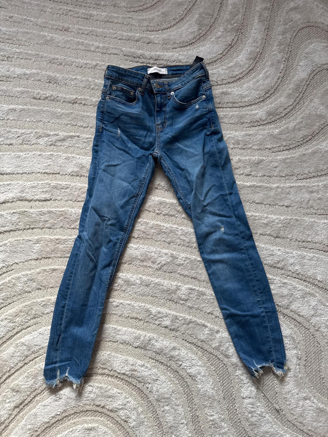Front view of blue jeans with front and back pockets, frayed hem.
