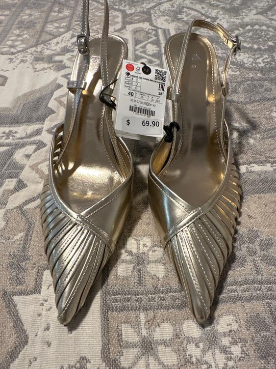 Gold high-heeled shoes with a braided design and a price tag of $69.90 on a geometric patterned surface.