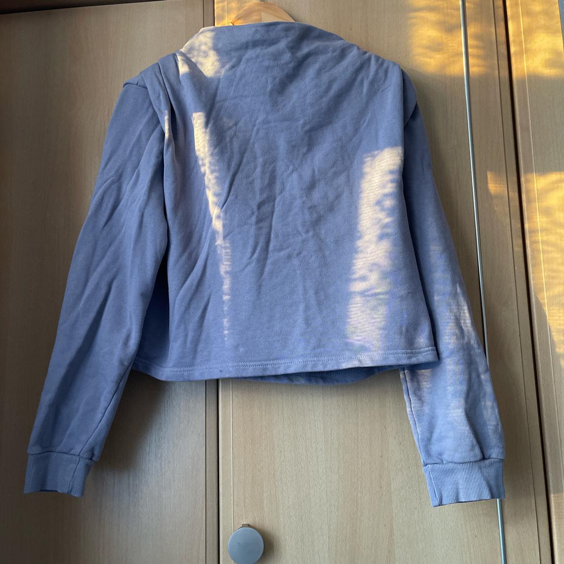 Light blue long-sleeved jacket hanging on a wooden hanger, with sunlight casting shadows on it and the wardrobe.