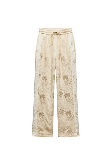 Front view of beige floral print trousers, elasticated waistband with drawstring.
