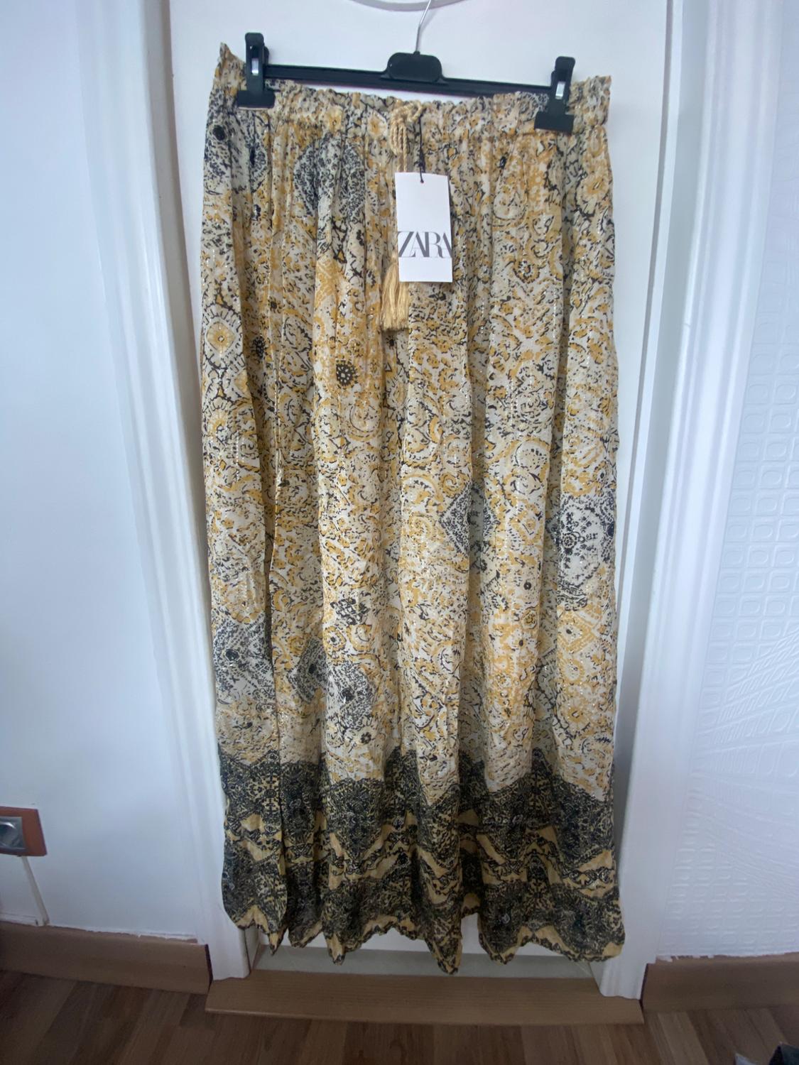 Long yellow and black patterned skirt hanging on a hanger. Visible label with the text "ZARA". White door background.
