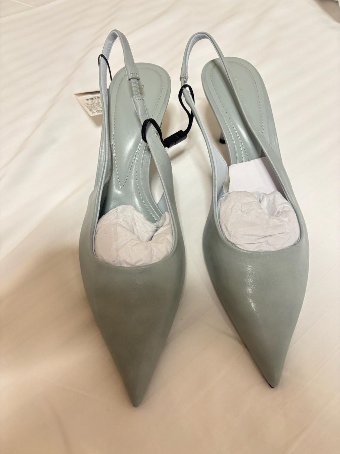 Light blue slingback high heels with a pointed toe on white fabric. They are stuffed with paper and have a tag hanging from them.